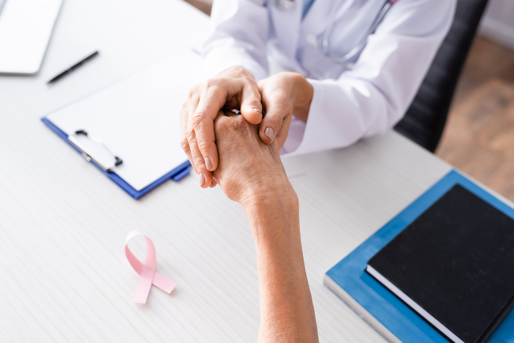 Enfoque selectivo del médico sosteniendo la mano del paciente cerca de la cinta rosa en la mesa - Foto, imagen