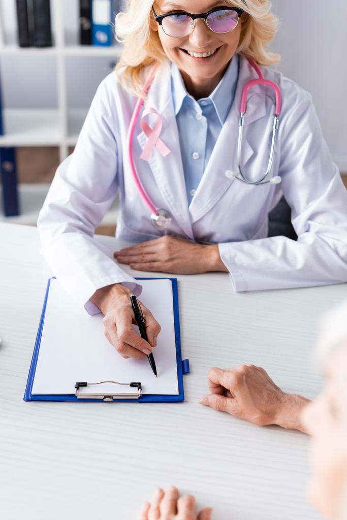 Enfoque selectivo del médico escribiendo en el portapapeles y mirando al paciente en la clínica - Foto, Imagen