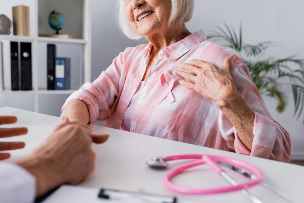 Vista recortada de una anciana con la mano cerca de la cinta rosa cerca del médico - Foto, Imagen