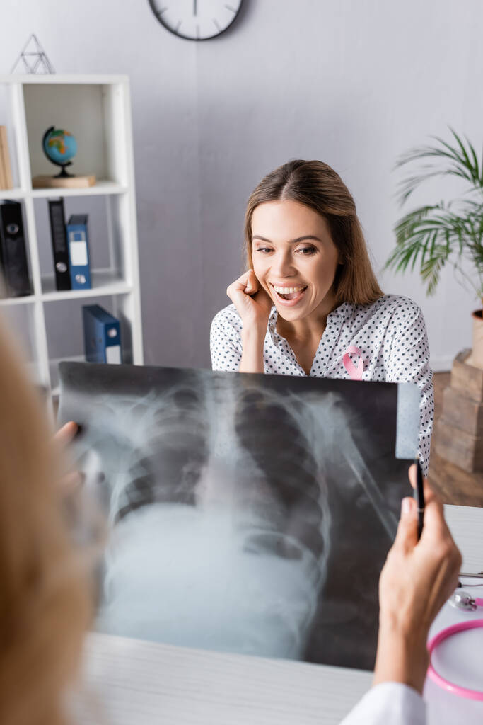 Selektiver Fokus einer jungen erwachsenen Frau, die mit einem Röntgenbild der Brust vor dem Arzt sitzt - Foto, Bild