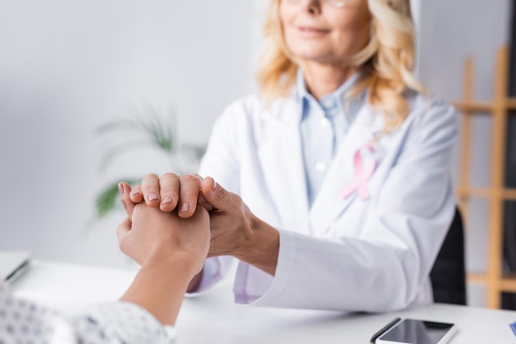 Concentration sélective du patient tenant la main avec un médecin près du smartphone sur le lieu de travail - Photo, image