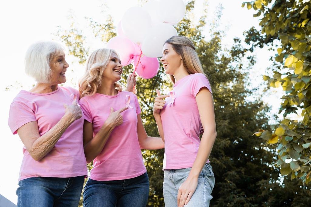 Низкий угол обзора женщин, указывающих пальцами на розовые ленты, держащих воздушные шары - Фото, изображение