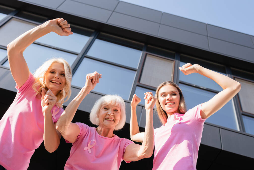 Χαμηλή γωνία άποψη των γυναικών σε ροζ t-shirts δείχνει τα χέρια και κοιτάζοντας την κάμερα - Φωτογραφία, εικόνα