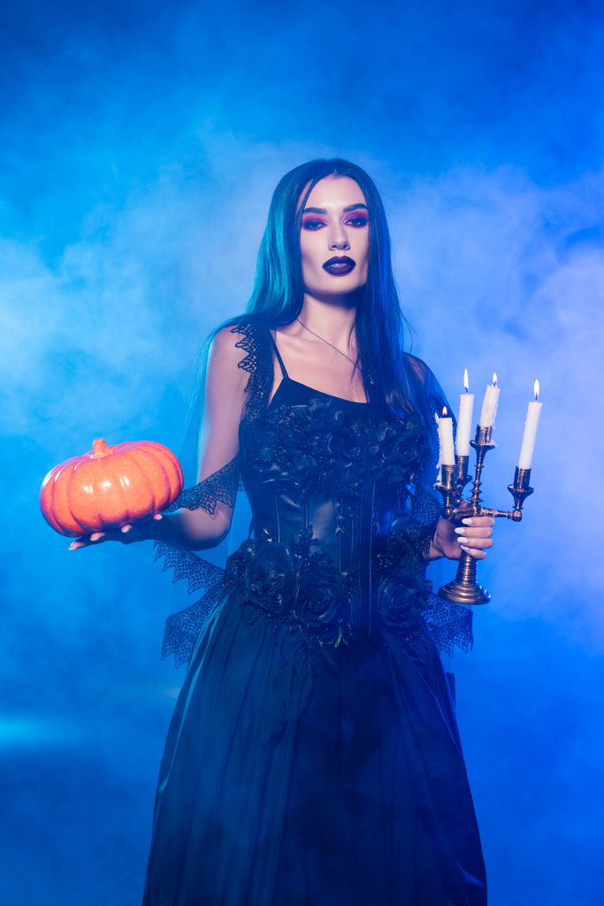 fiatal sápadt nő fekete ruhában kezében tök és égő gyertyák kék füst - Fotó, kép