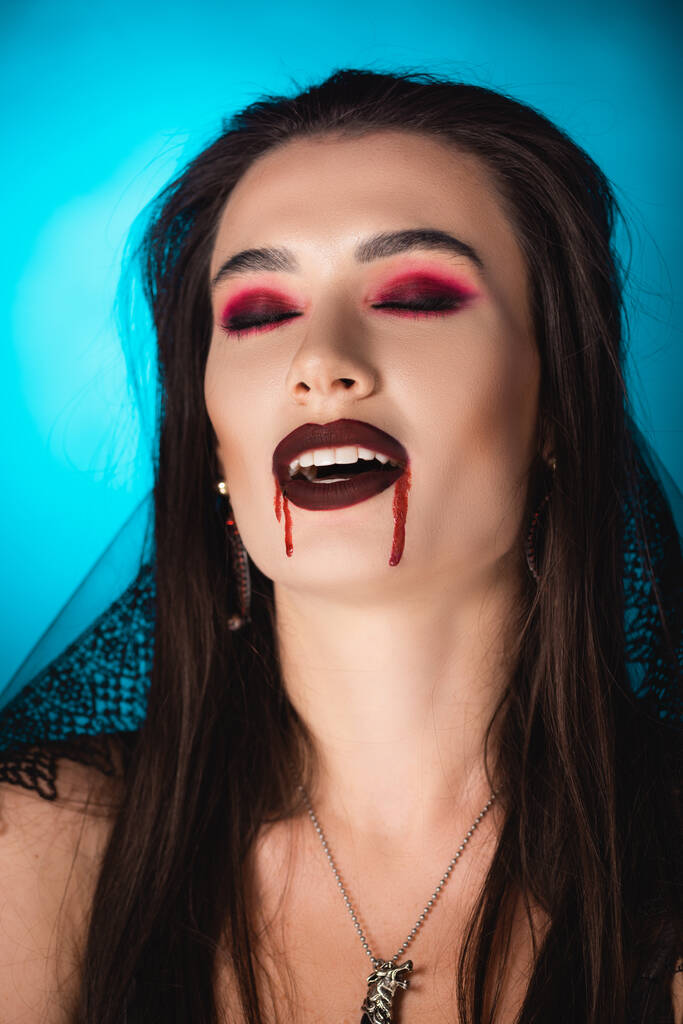 mladá žena v závoji, s krví na obličeji a zavřenýma očima na modrém - Fotografie, Obrázek