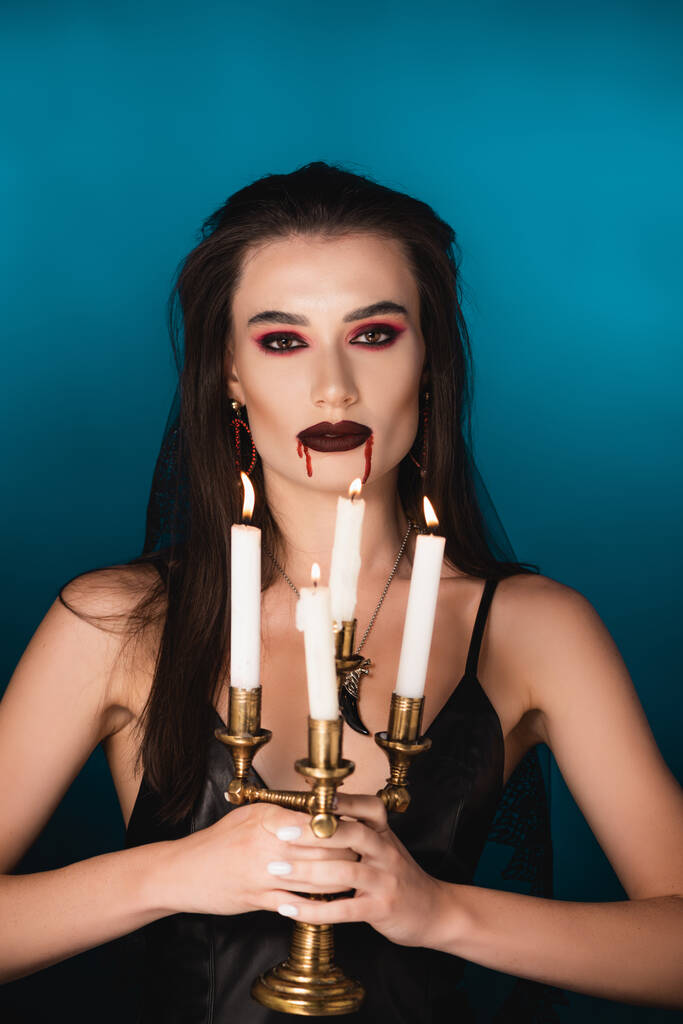 žena s krví na obličeji drží hořící svíčky na modré - Fotografie, Obrázek