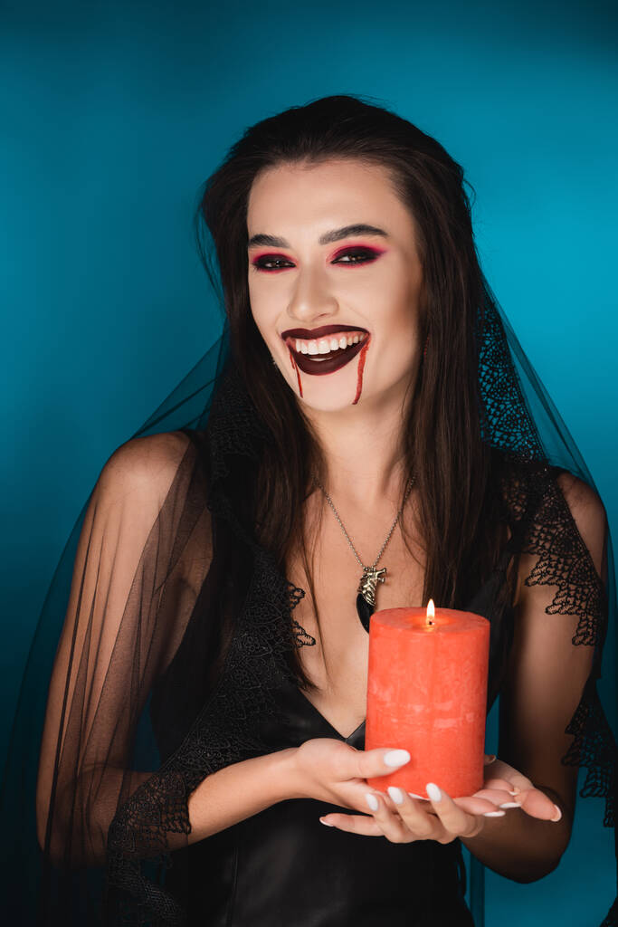 woman in veil with blood on face holding red burning candle and laughing on blue - Photo, Image