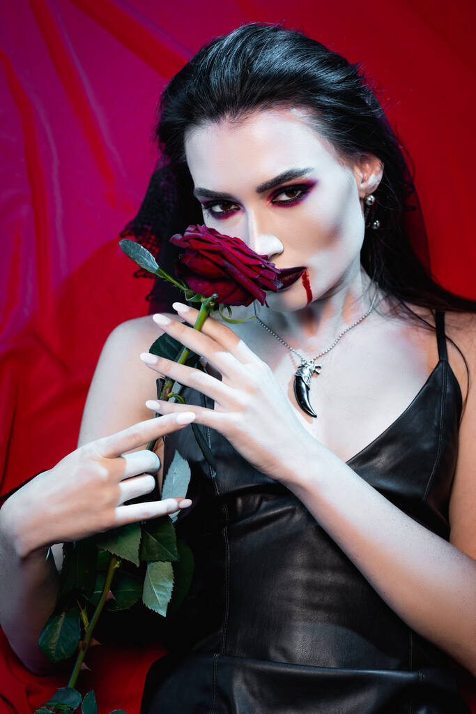 brunetka kobieta z krwi na twarzy patrząc w aparat i trzymając różę na czerwony - Zdjęcie, obraz