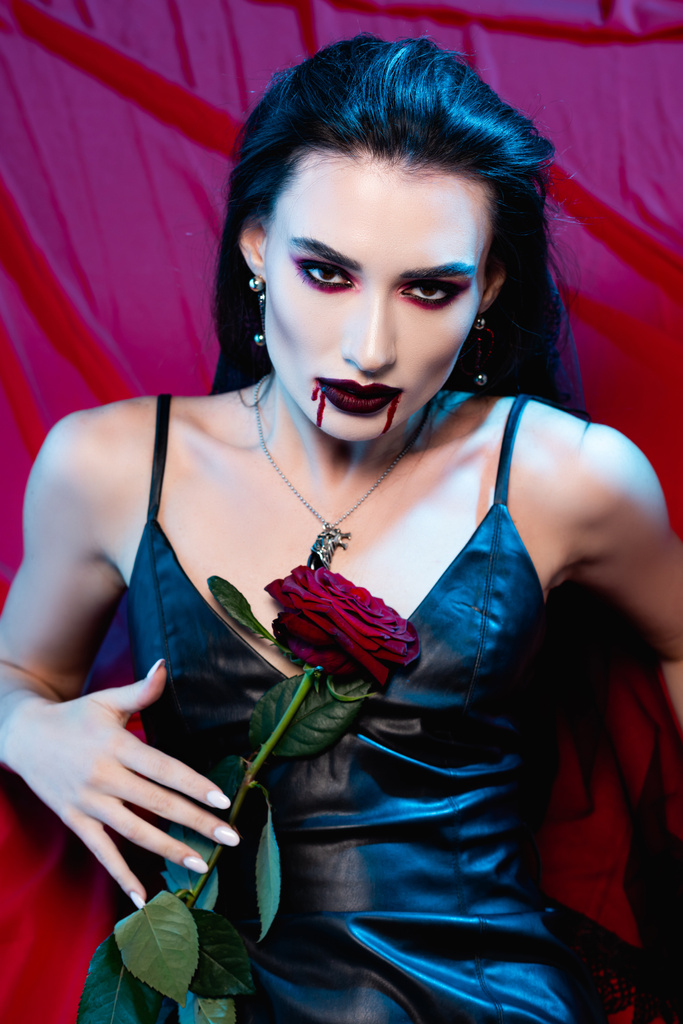 bledá žena s krví na tváři dívající se do kamery a držící růži na červené - Fotografie, Obrázek