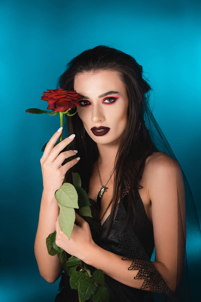 młoda kobieta z ciemnym makijażu gospodarstwa czerwona róża na niebiesko - Zdjęcie, obraz