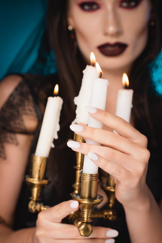 Selektiver Fokus einer blassen Frau mit schwarzem Make-up, die brennende Kerzen auf Blau berührt - Foto, Bild