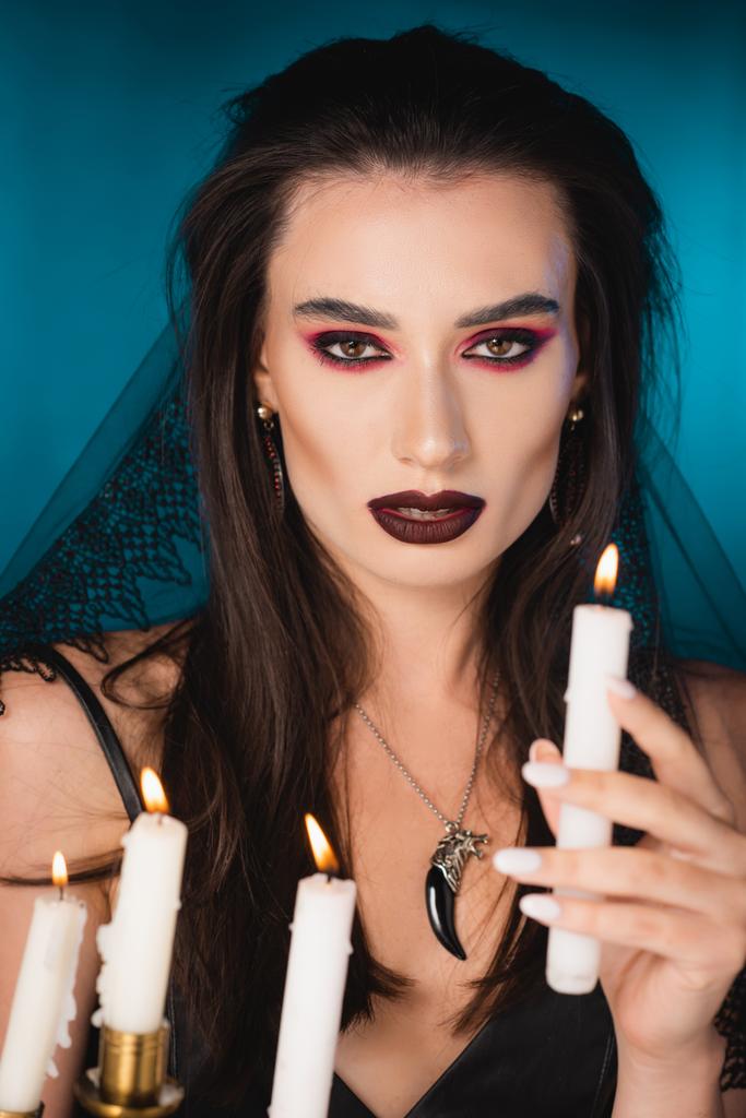 selective focus of pale young woman with makeup holding burning candle on blue - Photo, Image