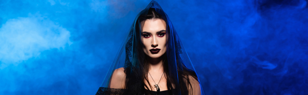 panoramic crop of woman in black veil on blue with smoke, halloween concept - Photo, Image