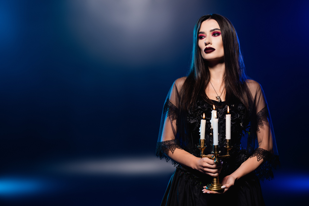 Nainen musta mekko ja huntu tilalla polttava kynttilöitä sininen, halloween käsite - Valokuva, kuva