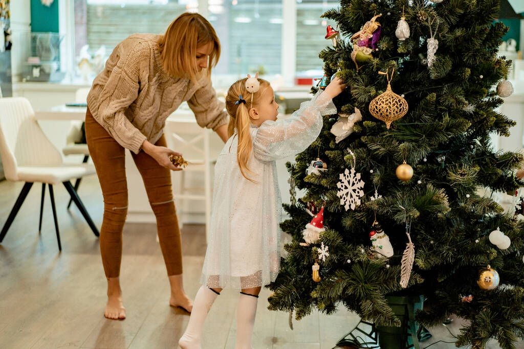 Maman et les enfants décorent le sapin de Noël avec des guirlandes et des jouets. La famille décore le sapin de Noël. Se préparer pour Noël et le Nouvel An. Les enfants se réjouissent devant l'arbre. - Photo, image