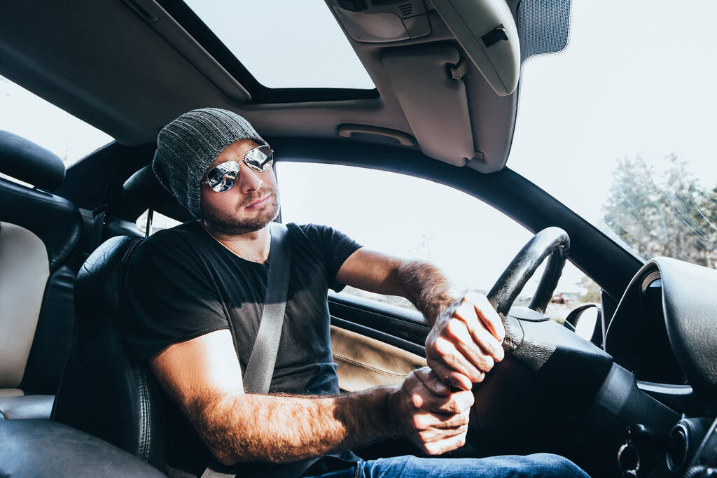Белый мужчина в очках и шляпе, управляющий мощным автомобилем, входит в поворот на скорости, крепко удерживая руль обеими руками - напряжение и концентрация во время вождения - Фото, изображение