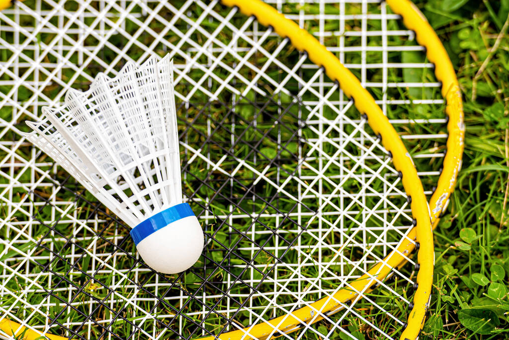 weißer Federball in Großaufnahme auf gelben Badmintonschlägern im grünen Gras, Ansicht von oben nach unten - Foto, Bild