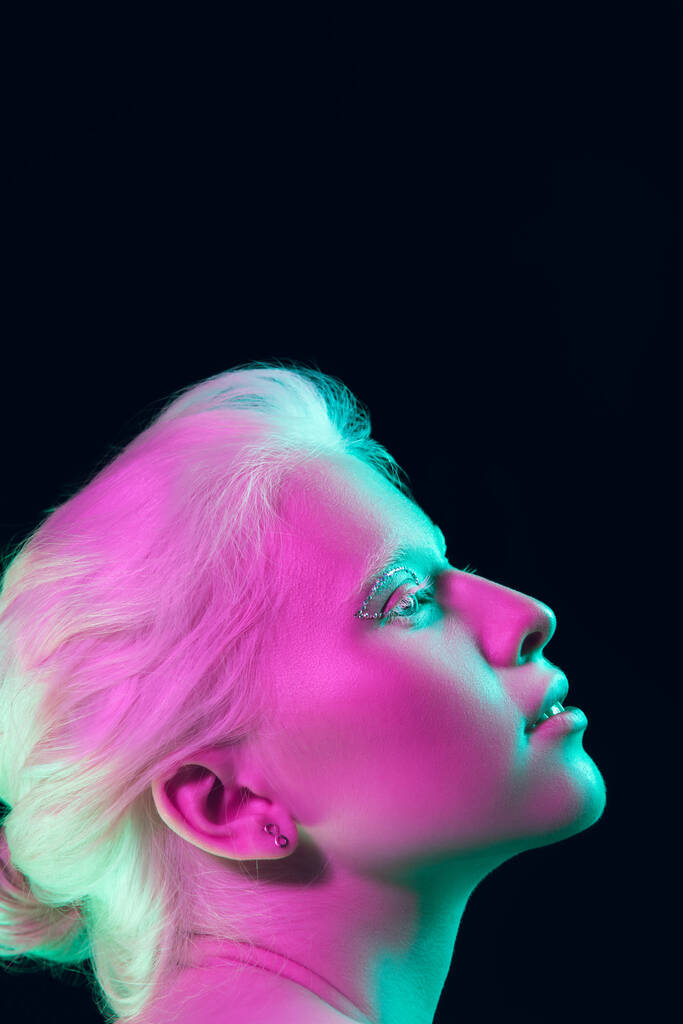 Portrait of beautiful albino girl isolated on dark studio background in neon light - Photo, Image