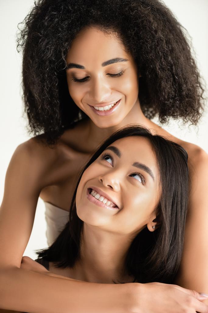gelukkig Afrikaans amerikaanse en aziatische vrouwen kijken naar elkaar geïsoleerd op wit - Foto, afbeelding