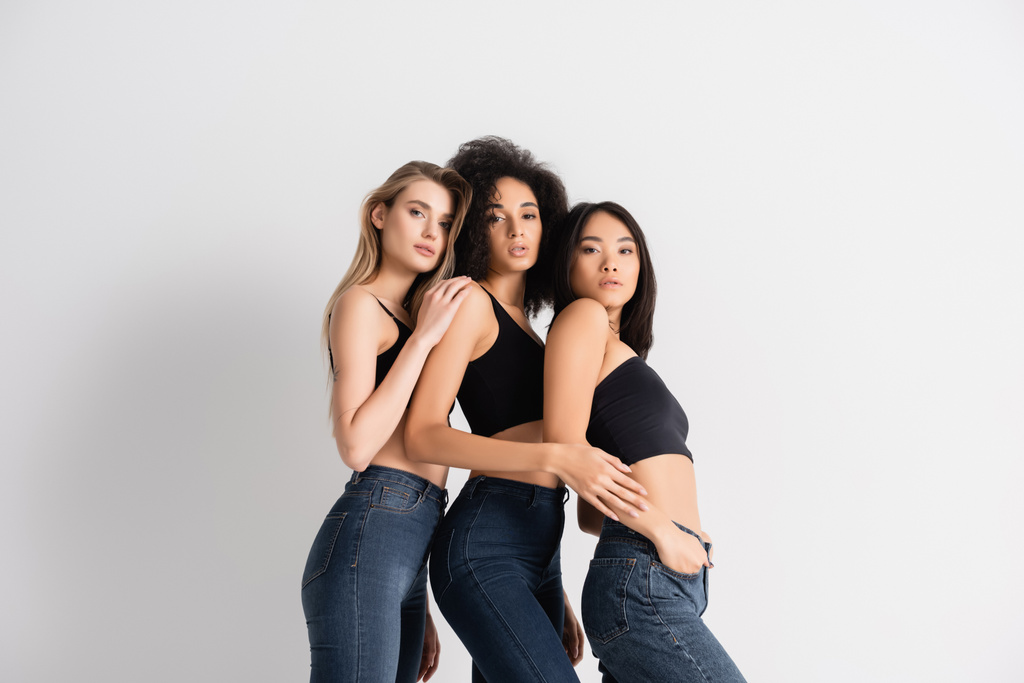 mulheres inter-raciais em tops e jeans jeans posando no branco - Foto, Imagem