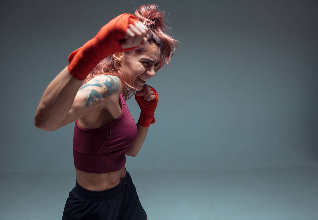 Спортивная девушка-боец тренируется в боксёрских бинтах изолированных на сером фоне. Женский спорт и мотивация - Фото, изображение