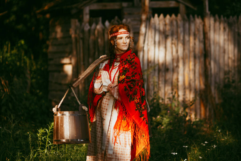 Όμορφη Σλαβική κοπέλα με μακριά ξανθά μαλλιά και καστανά μάτια σε λευκό και κόκκινο κεντημένο κοστούμι και ζυγό στους ώμους της.Παραδοσιακά ρούχα της Ουκρανικής περιοχής.καλοκαιρινή μέρα - Φωτογραφία, εικόνα