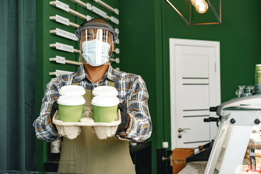 Працівник кав'ярні носить медичну маску, стоячи за лічильником у кафетерії
 - Фото, зображення