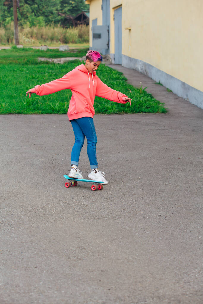 Стильна молода жінка з коротким волоссям верхи на синьому пластиковому скейтборді. Молодіжна концепція
. - Фото, зображення