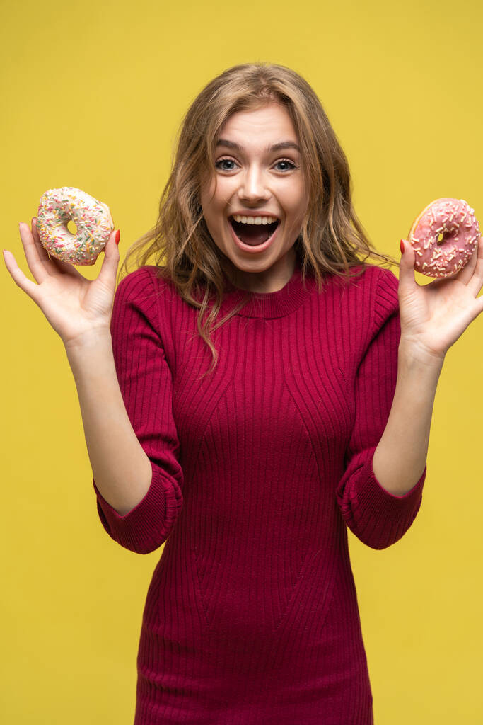 Porträt eines glücklichen Hipster-Mädchens, das sich für zwei Donuts entscheidet. Studioporträt auf gelbem Hintergrund. - Foto, Bild