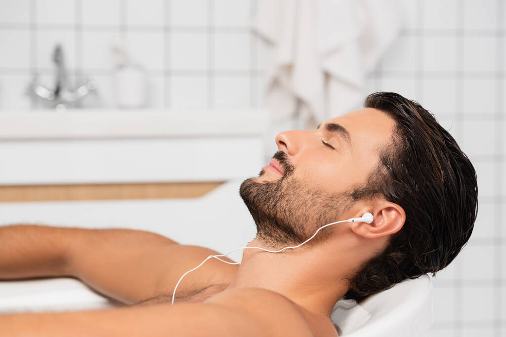 man met baard die muziek luistert in een oortelefoon in bad  - Foto, afbeelding