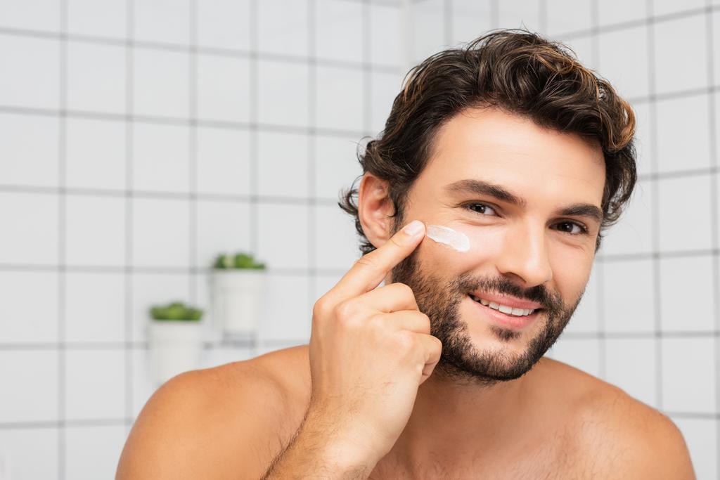 Mosolygós férfi alkalmazó kozmetikai krém az arcon a fürdőszobában  - Fotó, kép