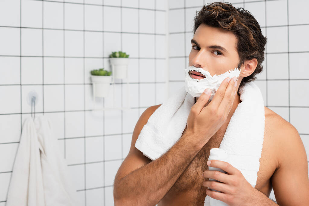 Izmos férfi törülközővel a nyaka körül alkalmazása borotválkozás hab a fürdőszobában  - Fotó, kép