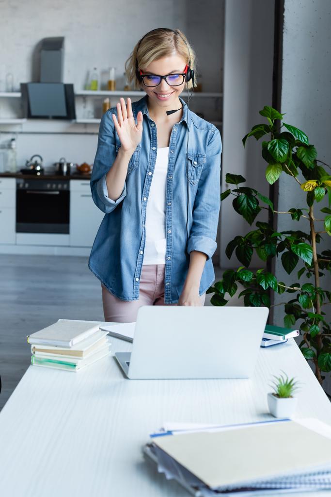 young blonde woman in eyeglasses having online conference and waving hand - Photo, Image