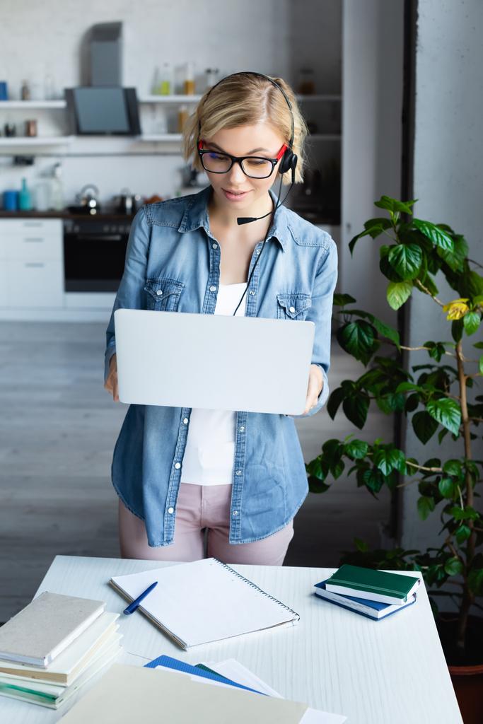 jong blond vrouw in bril werken vanuit huis en houden laptop - Foto, afbeelding