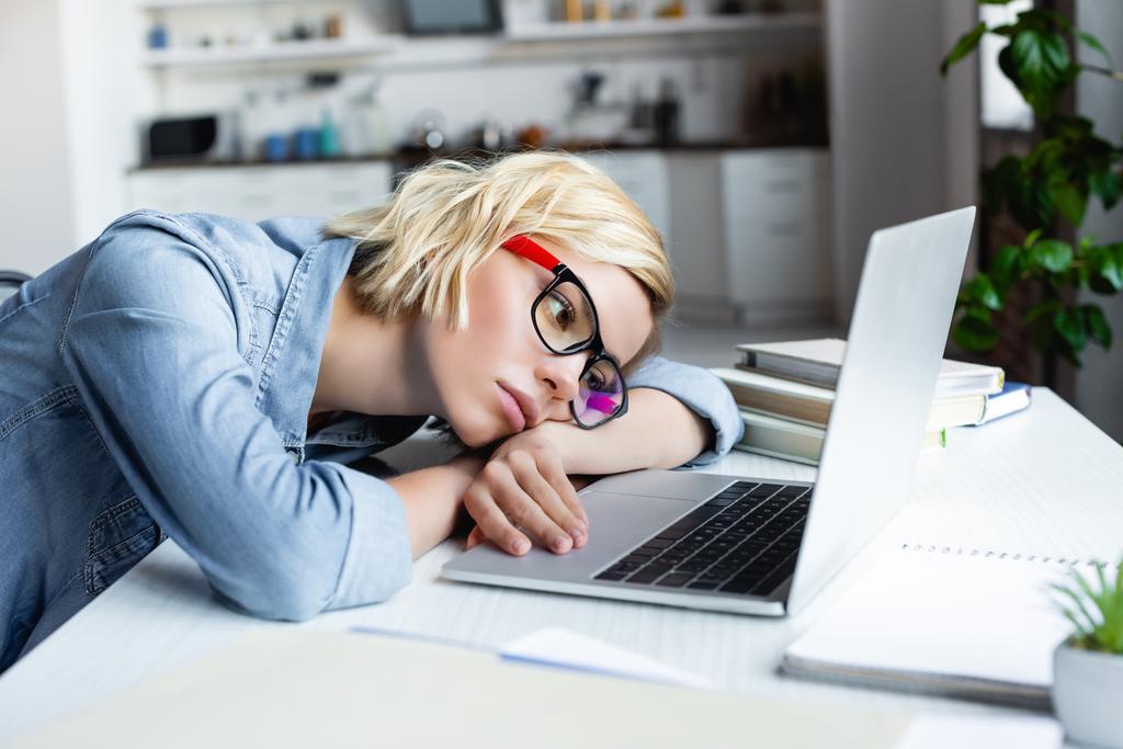 mujer rubia cansada en anteojos trabajando desde casa y acostada en la mesa  - Foto, imagen