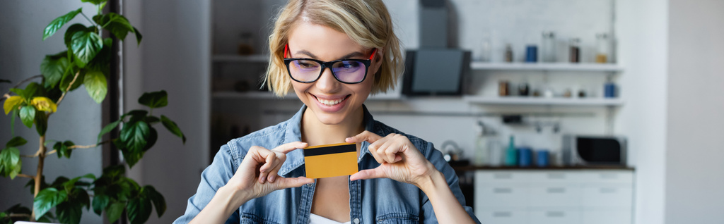 young blonde woman in eyeglasses holding credit card, horizontal banner - Fotoğraf, Görsel