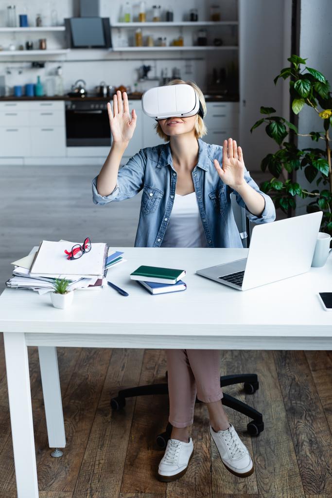 blonde woman in vr headset gesturing while sitting at table - Photo, Image