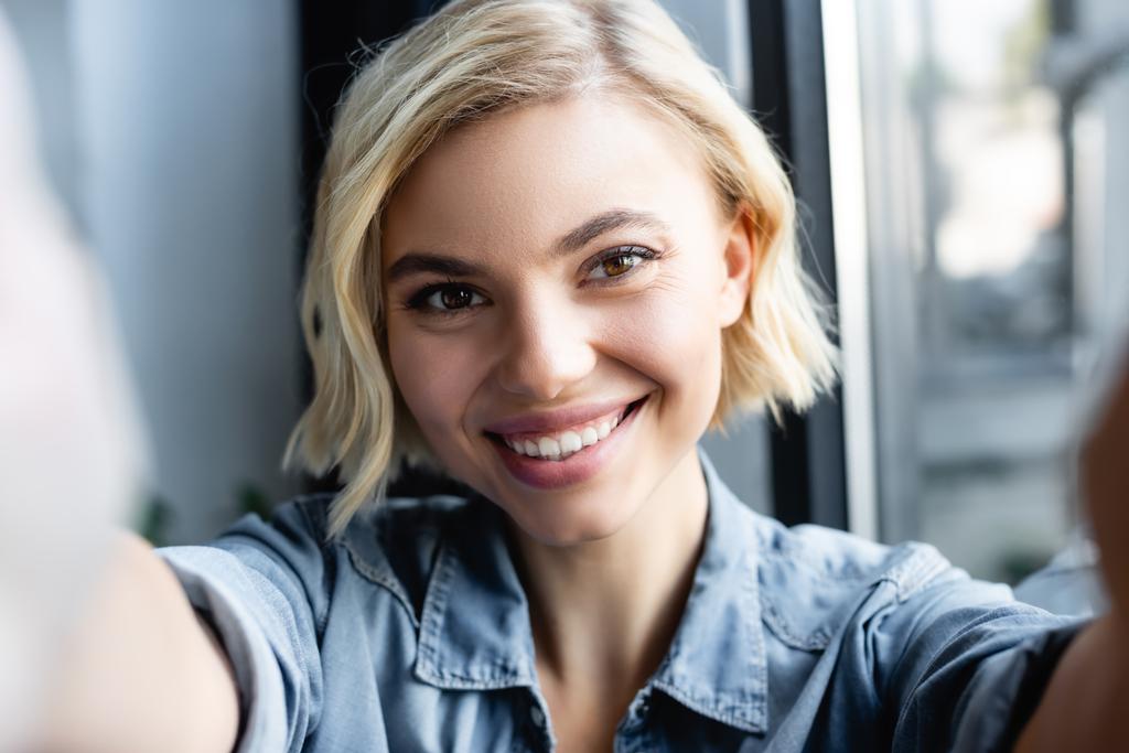 blonde woman smiling and looking at camera with blurred foreground - Photo, Image