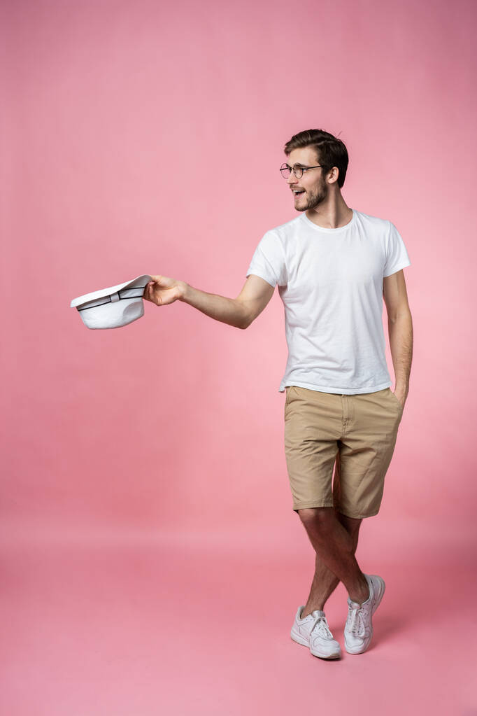 Happy attractive young man holding hat and asking for money over pink background. - Photo, Image
