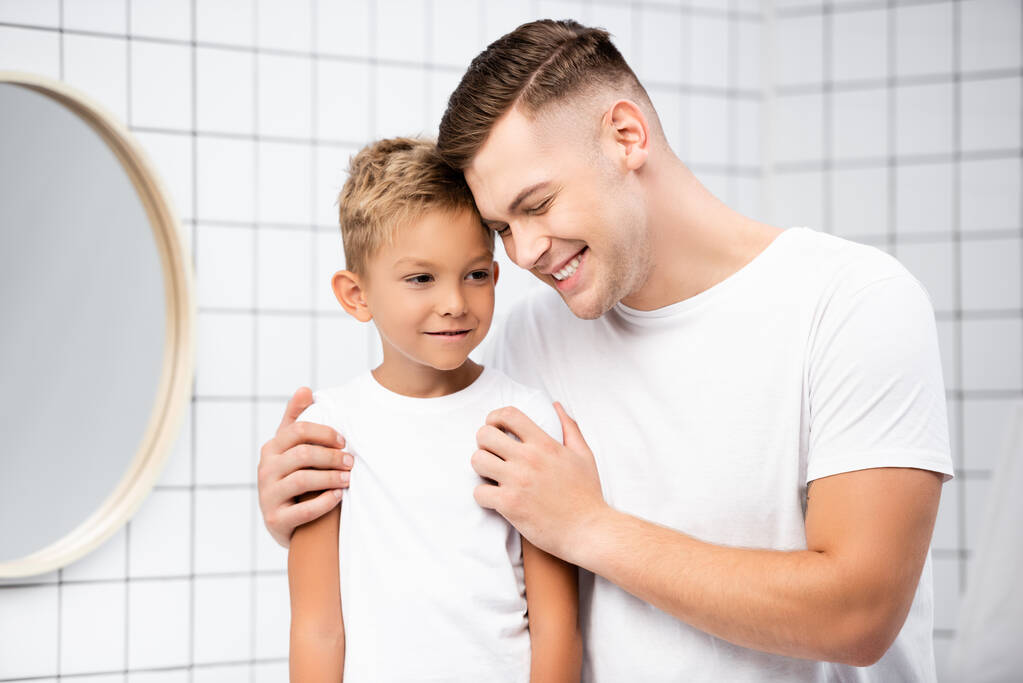 Усміхнений тато обіймає сина біля круглого дзеркала у ванній
 - Фото, зображення