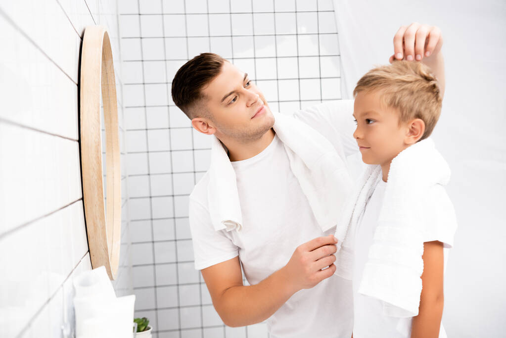 Pai com toalha no pescoço fixando o cabelo do filho olhando para o espelho no banheiro no fundo borrado  - Foto, Imagem