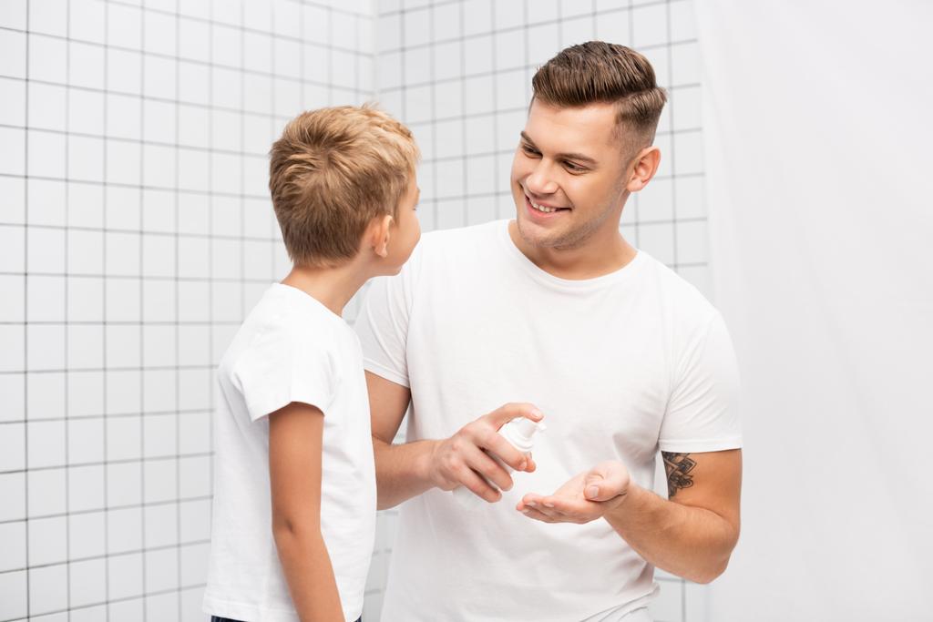 Улыбающийся отец смотрит на сына, сжимая пену для бритья в ванной - Фото, изображение