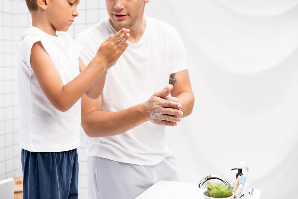 Padre e hijo frotando jabón entre manos mientras están de pie cerca del lavabo en el baño - Foto, imagen