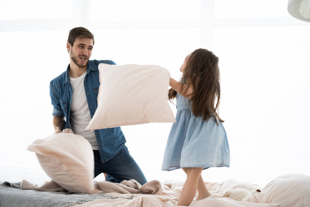 feliz padre e hija jugando pelea de almohadas en la cama por la mañana - Foto, Imagen