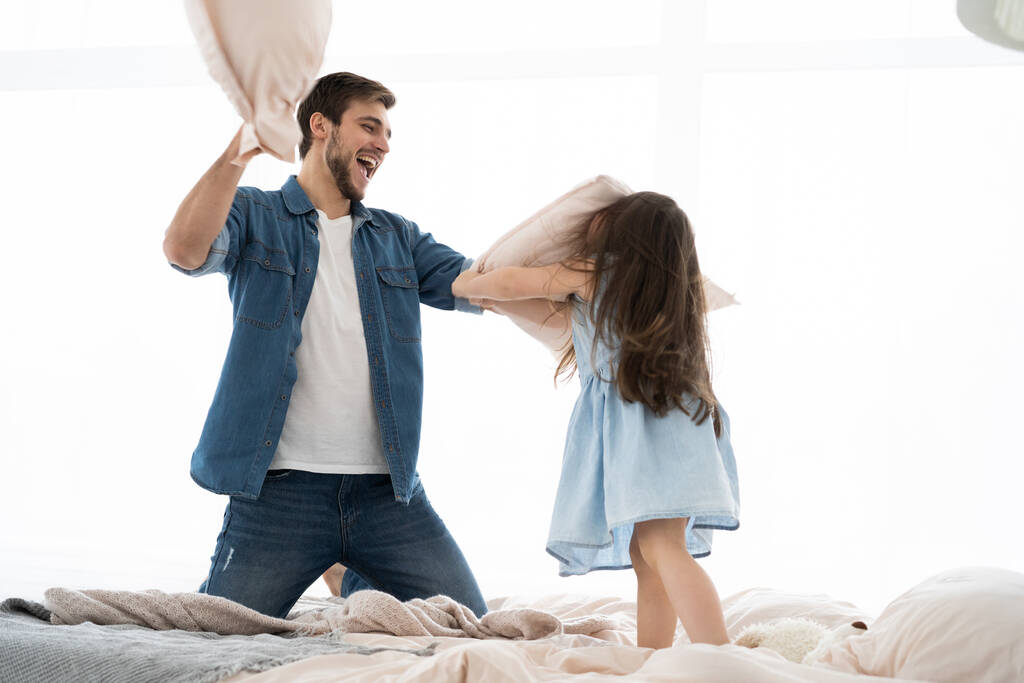 Ευτυχισμένος πατέρας και κόρη παίζουν μαξιλαροπόλεμο στο κρεβάτι το πρωί - Φωτογραφία, εικόνα