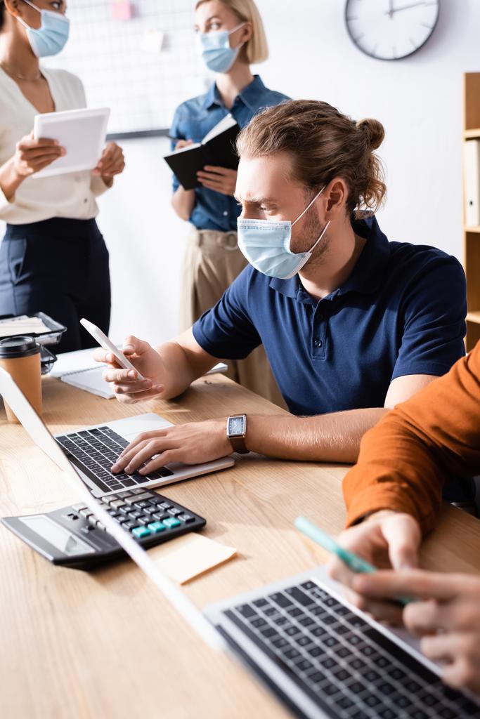 mladý tým multikulturních podnikatelů v lékařských maskách spolupracujících v otevřeném prostoru kanceláře - Fotografie, Obrázek