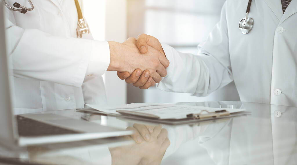 Twee dokters schudden elkaar de hand als overeenkomst over patiëntenbehandeling, close-up. Medische hulp, medisch concept - Foto, afbeelding