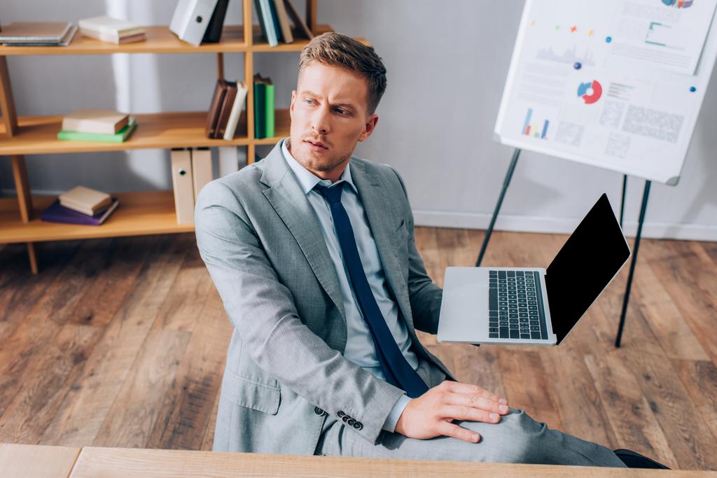 Jonge zakenman in pak houdt laptop met blanco scherm in kantoor  - Foto, afbeelding