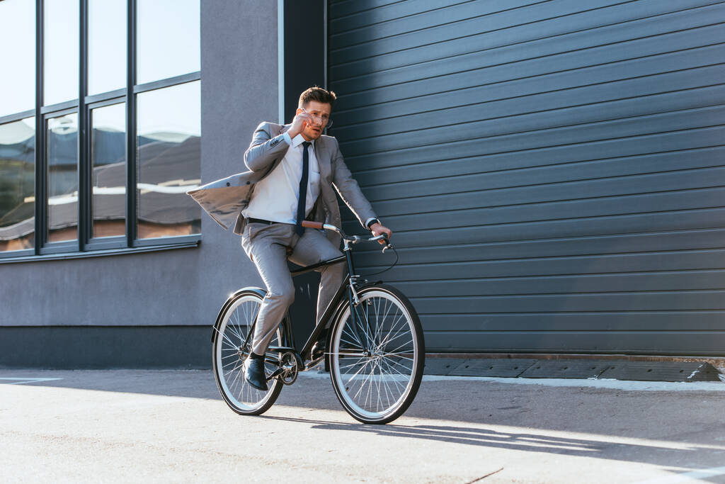 Zakenman in pak met bril tijdens het fietsen in de buurt van gebouw  - Foto, afbeelding