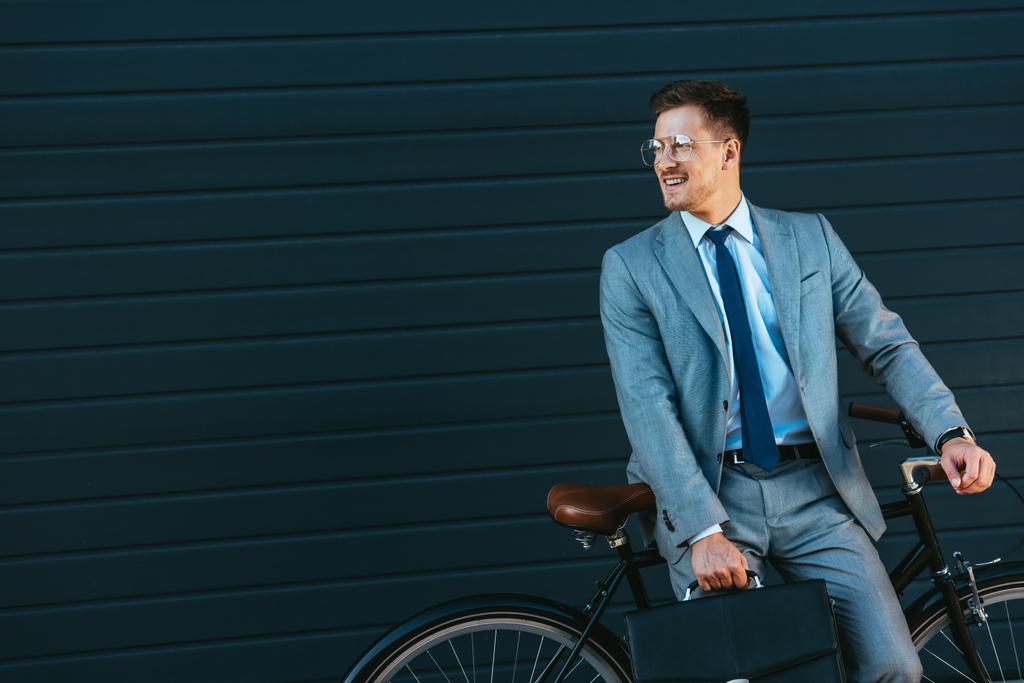 Hymyilevä liikemies salkku lähellä polkupyörän ja rakennuksen  - Valokuva, kuva